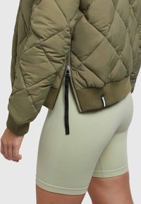 Olivovo zelená prešívaná puffa bunda s rebrovaným lemom a manžetami. Obsahuje bočný zips a štítok na leme, skombinovaná s svetlozelenými priliehavými šortkami.