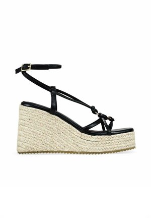 Sandalia cuña negra con tiras, hebilla en el tobillo y suela plataforma trenzada beige.