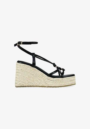 Sandalia cuña negra con tiras, hebilla en el tobillo y suela plataforma trenzada beige.