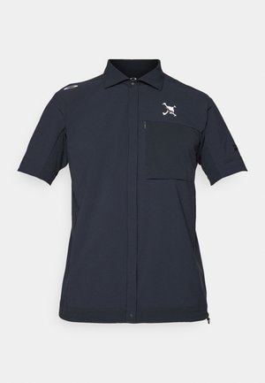 Kortærmet skjorte i mørk navy stof, med en frontlomme med lynlås, knaplukning og broderet logo på brystet.