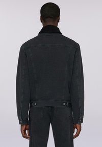Giubbotto in denim nero con colletto Sherpa, dotato di due tasche posteriori e bottoni in vita. Progettato con una vestibilità strutturata e cuciture minime.