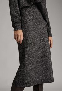 Grauer gestrickter Rock mit strukturierter Oberfläche, mittellang bis zur Wade. Verfügt über eine taillierte Passform und weichen, gemütlichen Stoff. Kombiniert mit einem dunklen Pullover.