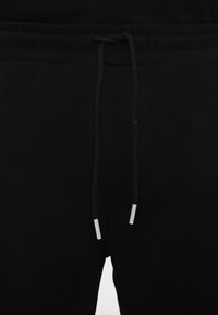Sorte sweatpants med elastisk talje, med snor og sølvfarvede metalspidser. Glat tekstur og enkelt design.