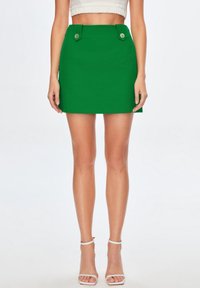 Vihreä mini-hame, jossa on muotoutuva istuvuus, ja vyötäröllä on kaksi koristeellista nappia. Sujuva kangas ja suora helma.