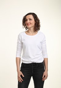 Weißes Langarm-T-Shirt mit Rundhalsausschnitt, kombiniert mit hoch taillierten schwarzen Jeans mit Knopfverschluss. Glatte Stoffoberfläche.