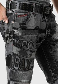 Jeans en denim noir et gris avec motif camouflage, tissu texturé, détails de couture et marquage en relief "CIPO" et "BAXX".