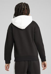 Sudadera negra con capucha ribeteada en blanco, con un corte relajado, puños y dobladillo acanalados. Tela suave y lisa con un diseño sencillo pero moderno.
