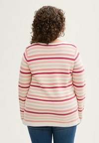 Gestreepte lange mouw top in lichtroze, rood en witte tinten. Geribbelde textuur, ontspannen pasvorm en ronde halslijn. Gecombineerd met blauwe jeans.