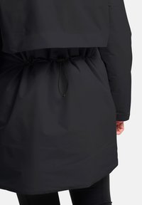 Zwarte parka met een getailleerde taille, voorzien van een zachte textuur, lange mouwen en knoopaccenten bij de manchetten.
