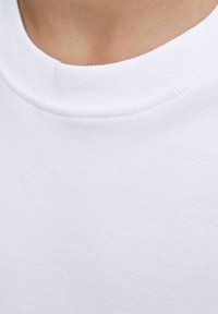 Gros plan sur une personne portant un T-shirt en coton blanc à col rond, en mettant l'accent sur le col et la partie supérieure de la poitrine.