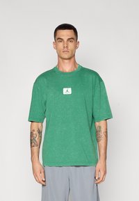 Grøn oversized T-shirt i slidt bomuld, med et lille hvidt mærke med et jumpman logo i midten. Korte ærmer og rund halsudskæring.