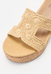 Gewebte beige Riemensandale mit floralen Details, texturiertem Riemen und einer natürlichen Korkplattformsohle. Die glatte Fußbett sorgt für zusätzlichen Komfort.