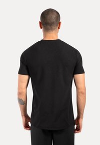 Camiseta negra de manga corta hecha de algodón, con diseño de cuello redondo, textura suave y forma ajustada, vista desde la parte de atrás.