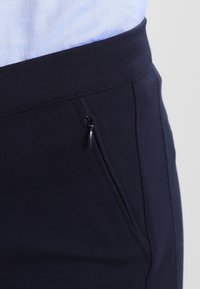 Mörk marinblå byxor gjorda av stretchigt material, med en dragkedjeficka på höger sida och en slät midja.