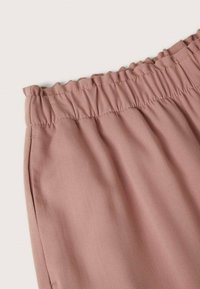 Jasnoróżany elastyczny pasek w talii z subtelną fakturą. Materiał wydaje się miękki i lekko luźny, oferując swobodny krój. Brak widocznych wzorów lub elementów metalowych.