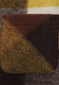 Tessuto di lana con un motivo geometrico nei colori marrone, giallo senape e grigio. Presenta una piccola tasca rettangolare con bordi cuciti.