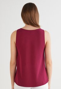 Ärmelloses Top in Burgunderrot mit rundem Ausschnitt, glatter Textur und lockerem Schnitt. Der Rücken ist mit einem geschwungenen Saum versehen.