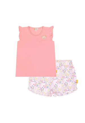 Rosa Oberteil mit Rüschensäumen und Bären-Patch, kombiniert mit weißen Shorts, die ein florales Muster in Pink, Gelb und Blau aufweisen.