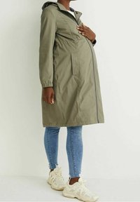 Gravidkappa i olivgrön, med dragkedja fram, två sidofickor, elastiska ärmslut och huva. Bärs över blåjeans och sneakers.
