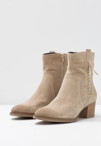 Beżowe zamszowe botki za kostkę z bocznym zamkiem i plecionym detalem. Solidny, blokowy obcas oraz gładka tekstura z zaokrąglonym noskiem.