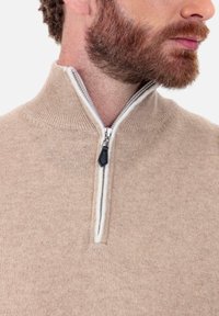 Beiger Reißverschluss-Pullover mit einem Trichterkragen. Weiche Textur, kontrastierendes weißes Futter und ein kleiner schwarzer Reißverschlussgriff als Akzent.