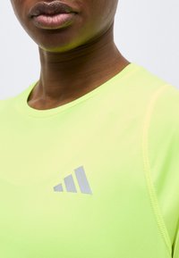 Κοντινό πλάνο ενός ατόμου που φοράει αθλητική μπλούζα νέον κίτρινου χρώματος με ανακλαστικό λογότυπο τριών γραμμών στο στήθος.