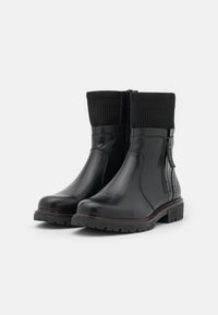 Schwarze Lederstiefeletten mit gerippten Strickbündchen, seitlichen Reißverschlüssen und einer strukturierten Sohle mit roter Naht entlang der Kante.