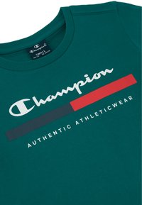 Camiseta de algodón en color verde azulado con un logo blanco de "Champion", rayas horizontales en gris oscuro y rojo, y el texto "AUTHENTIC ATHLETICWEAR" debajo.