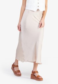 Gonna midi in seta beige chiaro con un design fluido e orlo asimmetrico, abbinata a sandali platform marroni con cinturino a fibbia.