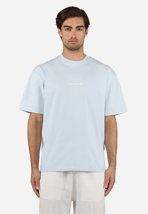 T-shirt en coton bleu clair à manches courtes, col rond, avec le logo "PEGAD0R" en blanc sur le devant. La coupe est décontractée avec une texture lisse.