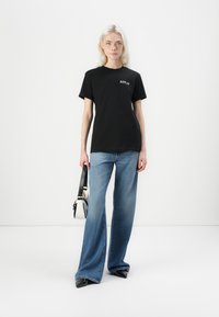 Black cotton t-shirt with "REPLAY" logo, paired with wide-leg blue jeans. Model holds a small black and white handbag. Smooth texture.