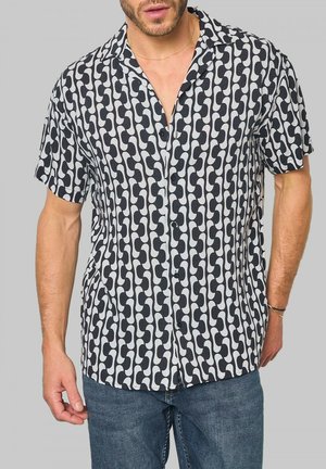 Chemise à manches courtes à motif noir et blanc présentant des formes abstraites, fermeture par bouton et coupe décontractée. Le tissu semble léger et texturé.