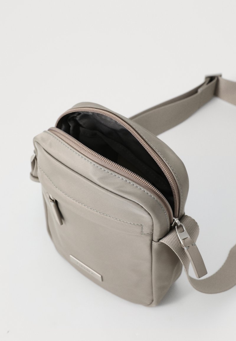 Borsa a tracolla grigia realizzata in tessuto morbido, con scomparto principale con zip e tasca frontale, tracolla regolabile e branding sottile.