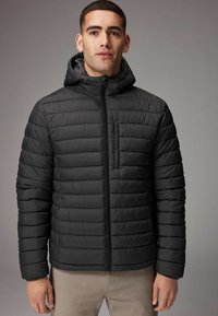 Jachetă neagră, umplută, cu un design cu matlasare orizontală, glugă atașată, fermoar frontal complet și un buzunar pe piept cu fermoar. Material sintetic neted.