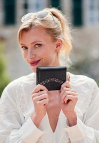 Black leather wallet with a textured wave design featuring polka dots in pink, white, and blue. Compact shape with a smooth surface and branding.
