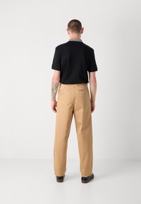 Black polo shirt with a patterned collar, paired with tan wide-leg trousers and black shoes, viewed from the back. Simple and minimal design.