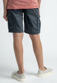 Tummanharmaat cargo-shortsit, joissa on useita sivutaskuja, kevyttä kangasta ja rento istuvuus, yhdistettynä vaaleanharmaisiin slip-on-kengiin.