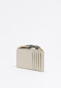 Portafoglio beige realizzato in pelle liscia, dotato di sei slot per carte, un accento metallico e una tracolla decorativa intrecciata.