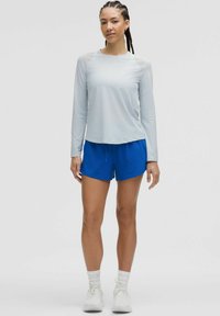 Camisa de manga larga azul clara con una textura suave, combinada con unos pantalones cortos azules. El conjunto se completa con zapatos deportivos blancos y calcetines.