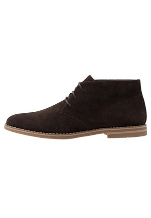Botas de ante marrón oscuro para hombre, con cordones y suela de goma color cuero, vista lateral sobre fondo blanco.