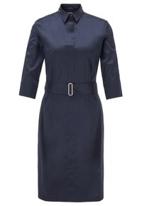 Granatowa sukienka koszulowa z gładkiego materiału, z kołnierzykiem, rękawami o długości trzech ćwiartek oraz paskiem w talii z prostokątną klamrą.
