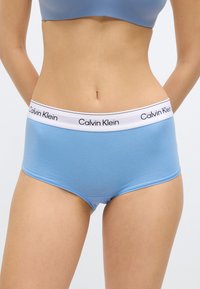 Ανοιχτό μπλε βαμβακερά σορτσάκια για αγόρια με λευκή ελαστική μέση που φέρει μαύρη επιγραφή «Calvin Klein». Λείο ύφασμα, εφαρμοστή σχεδίαση.