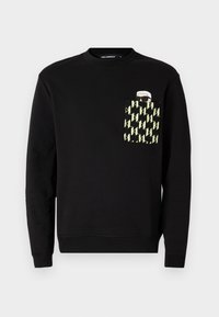 Sort sweatshirt med rund hals, der har en lomme med et gult og sort geometrisk mønster samt et trykt grafisk motiv på lommen.