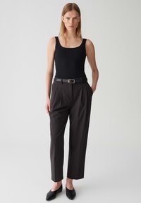 Un débardeur noir associé à un pantalon taille haute gris foncé et une ceinture noire. Tenue complétée par des ballerines noires à bout pointu. Textures de tissu lisses.