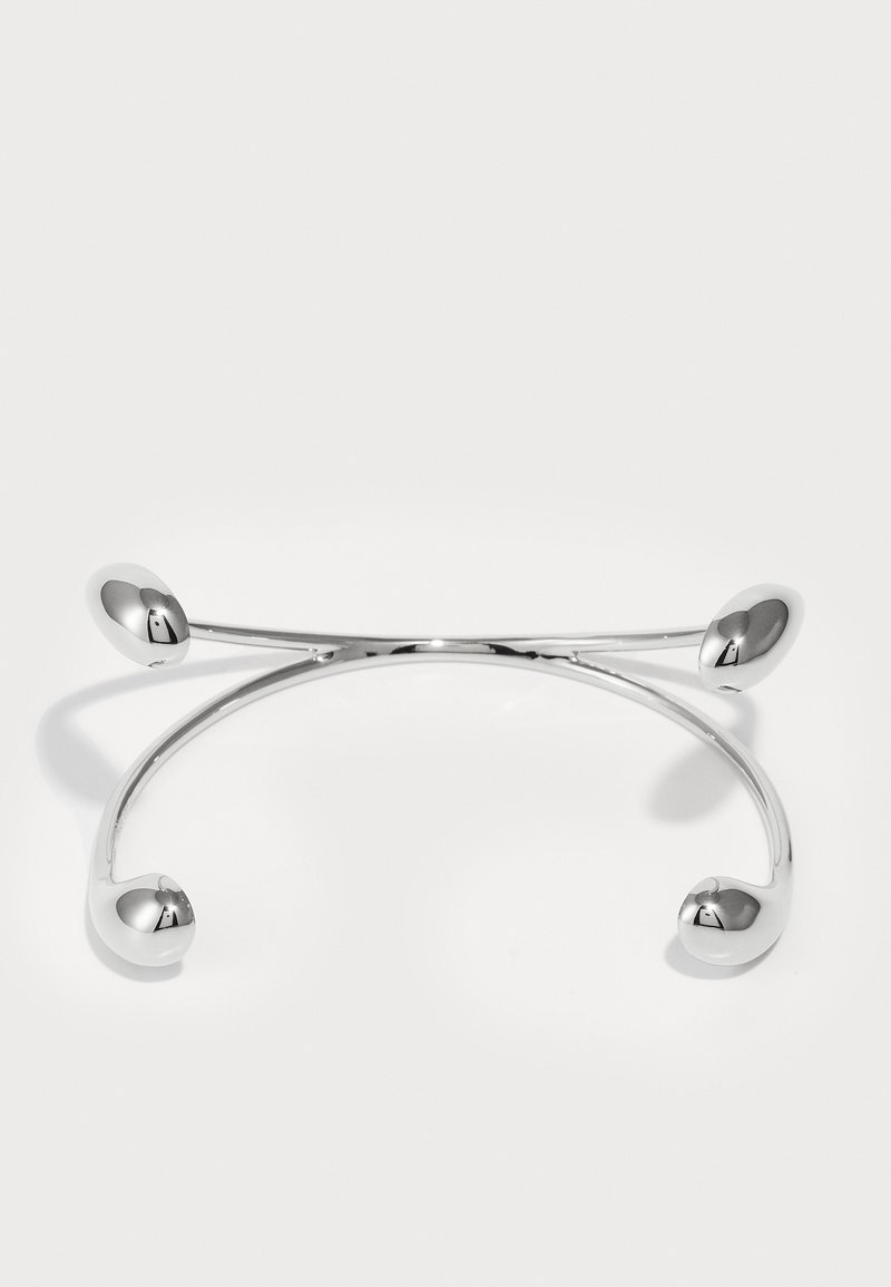Ασημένια μεταλλική βραχιόλι με καμπύλη σχεδίαση, που διαθέτει τρία στρογγυλά άκρα. Λείος, ανάκλασης επιφάνεια με γυαλισμένη φινίρισμα.