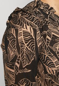 Svart skjorta med ett bladmönster i beige. Tyget är lätt och har en volangkrage samt texturerade detaljer på axeln.