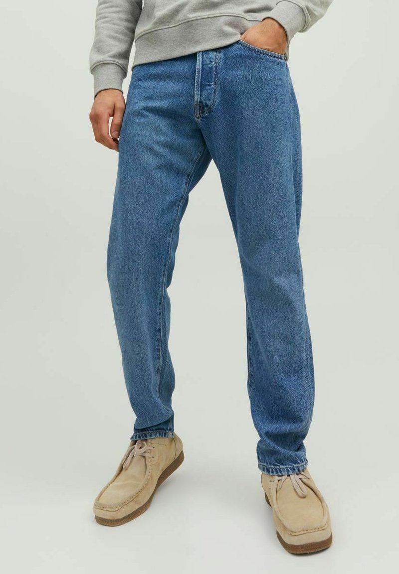 Jeans in denim azzurro chiaro con vestibilità rilassata, design a cinque tasche e cuciture visibili, abbinati a scarpe in suede beige.