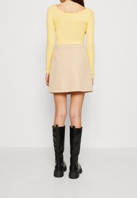 Top amarillo de manga larga con escote en la espalda, combinado con una falda beige clara. Botas negras hasta la rodilla con acabado texturizado y suelas gruesas.