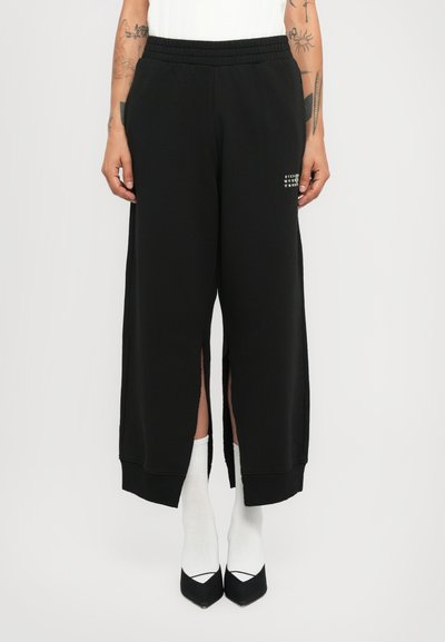 Pantalons de jogging noirs avec fentes latérales, taille élastique et un imprimé graphique subtil. Fabriqués en tissu doux, conçus pour le confort et le mouvement.