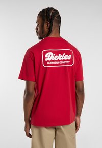 Camiseta de algodón roja con una etiqueta de logo blanca "Dickies WORKWEAR COMPANY" en la parte de atrás. Diseño de mangas cortas y cuello redondo.